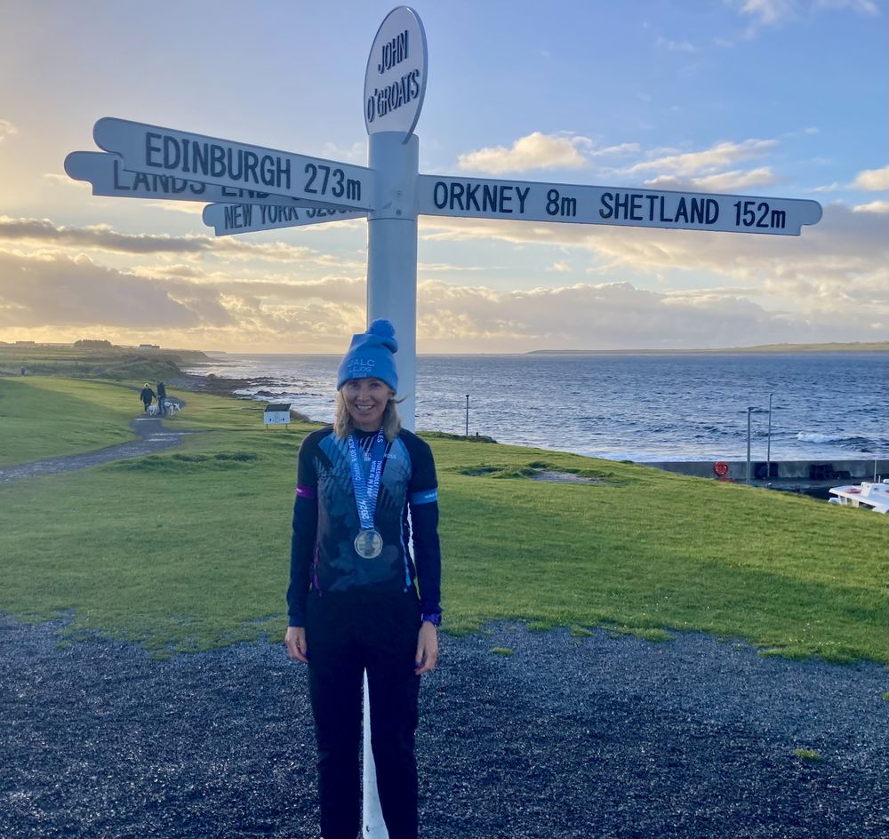Juliet wearing a medal at the John o' Groats signpost at sunset